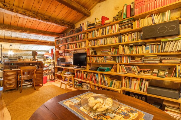 Una habitación acogedora con estanterías de madera llenas de libros y un televisor. Hay un escritorio de madera con una silla, una mesita con un cuenco y una alfombra en el suelo.