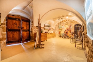 Une pièce aux murs de pierre, aux portes en bois, avec un vélo et un tableau accroché au mur.