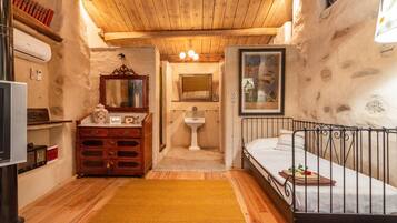 A rustic room with a wooden ceiling, a bed, a dresser, a mirror, a sink, and a television.