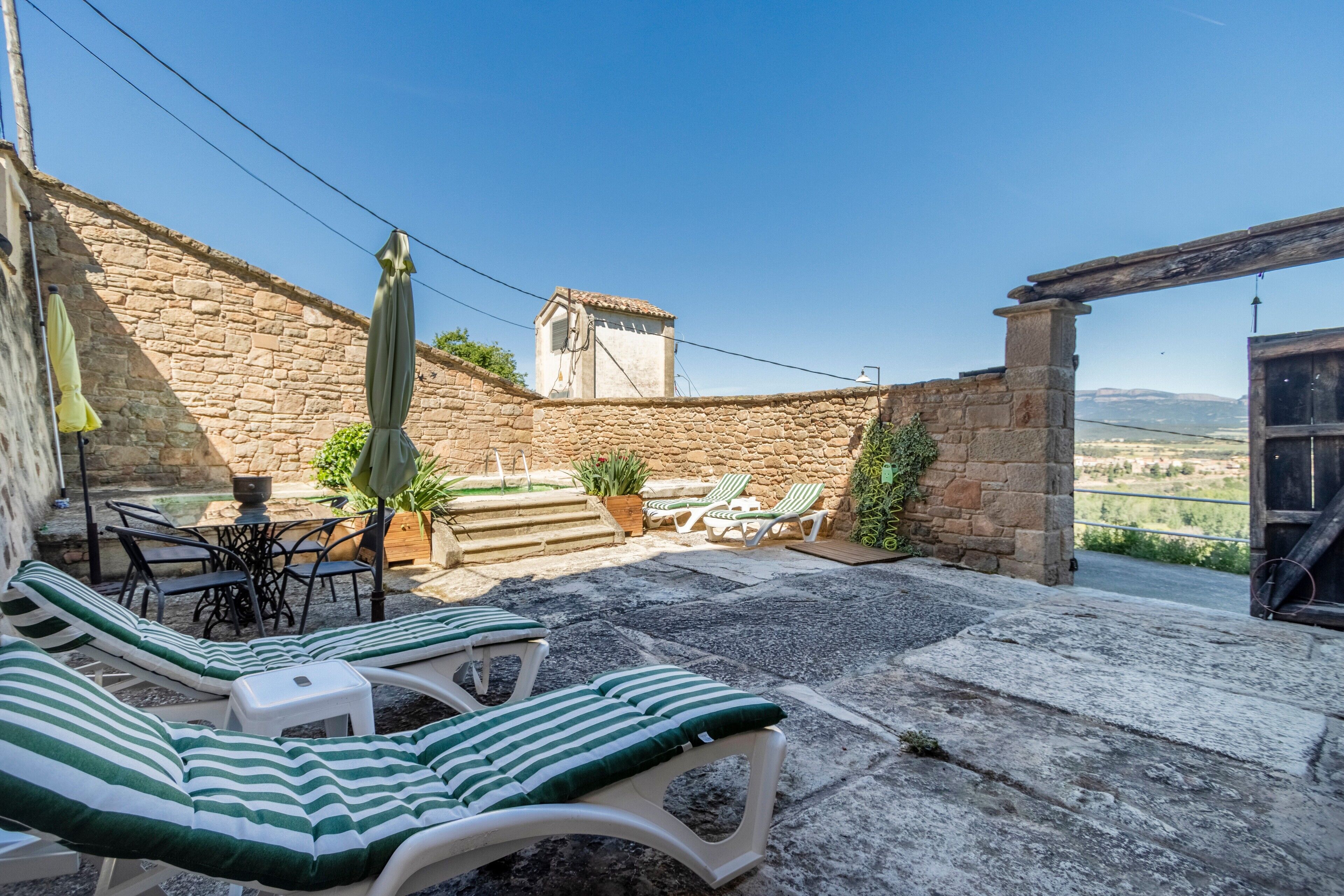 Un patio con paredes de piedra, sillones, una mesa y una sombrilla.
