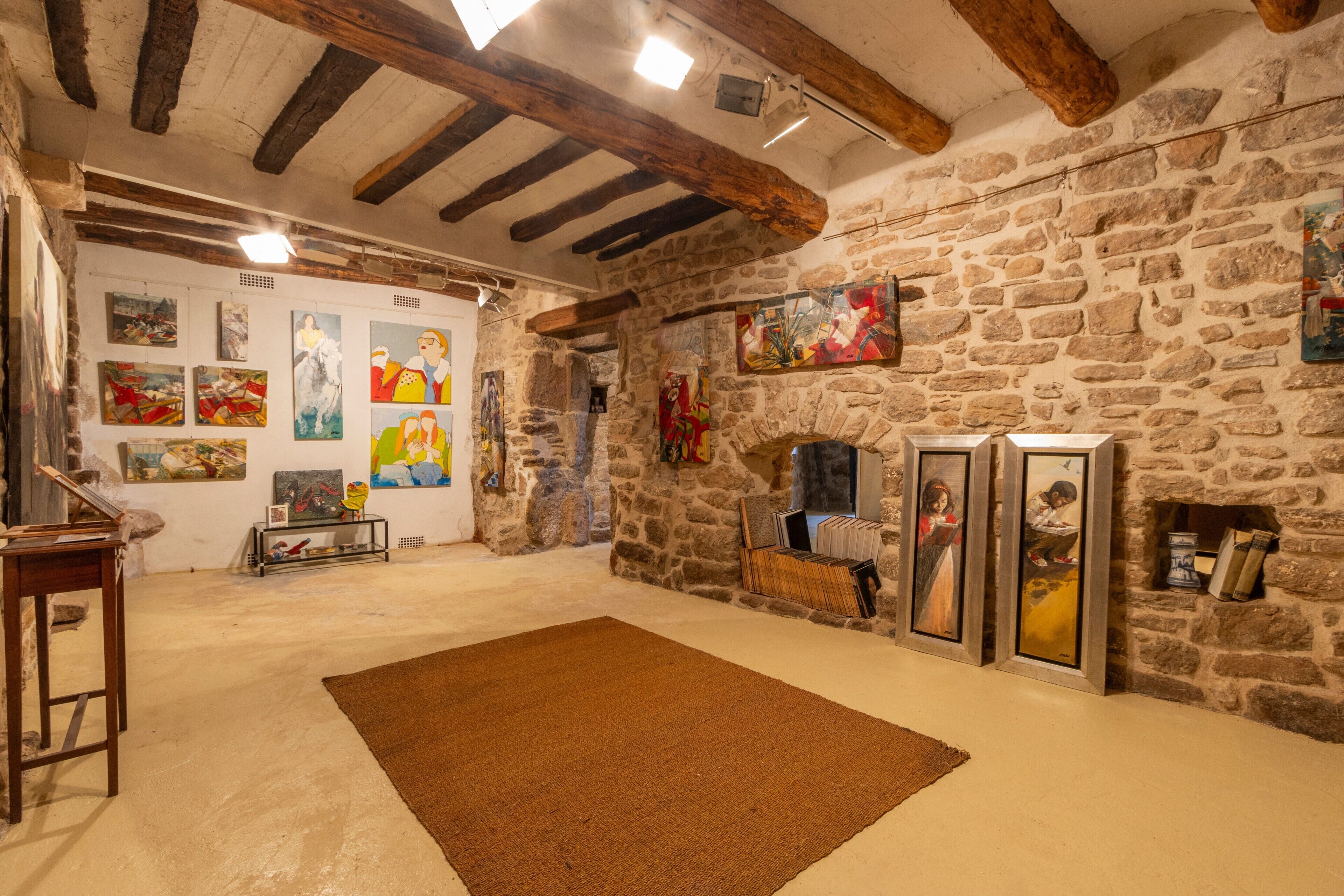 Una habitación con vigas de madera a la vista, paredes de piedra y obras de arte en las paredes.