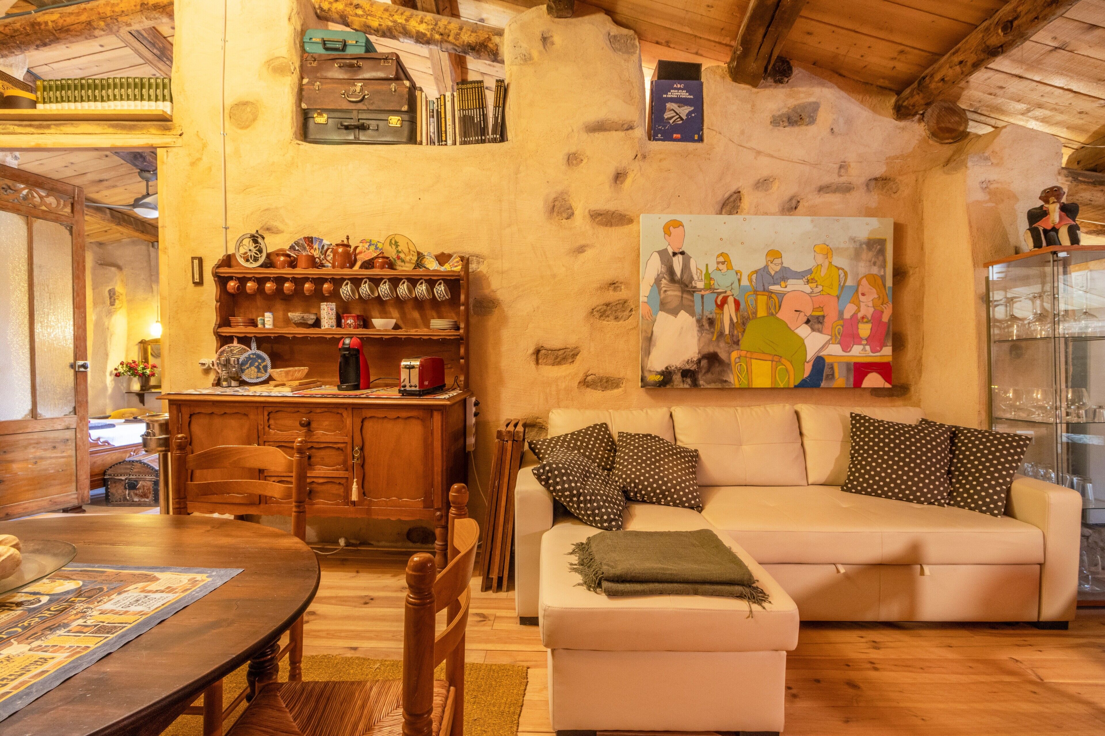 Un accogliente soggiorno con tavolo da pranzo in legno, divano con cuscini decorati, un quadro appeso e una parete in pietra.