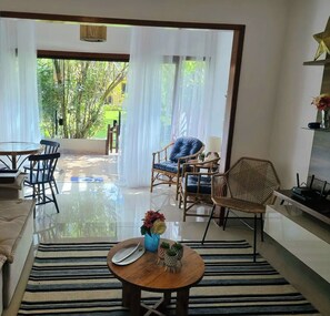 Ein Wohnzimmer mit Sofa, Sesseln, Couchtisch und Blick auf Grünflächen.