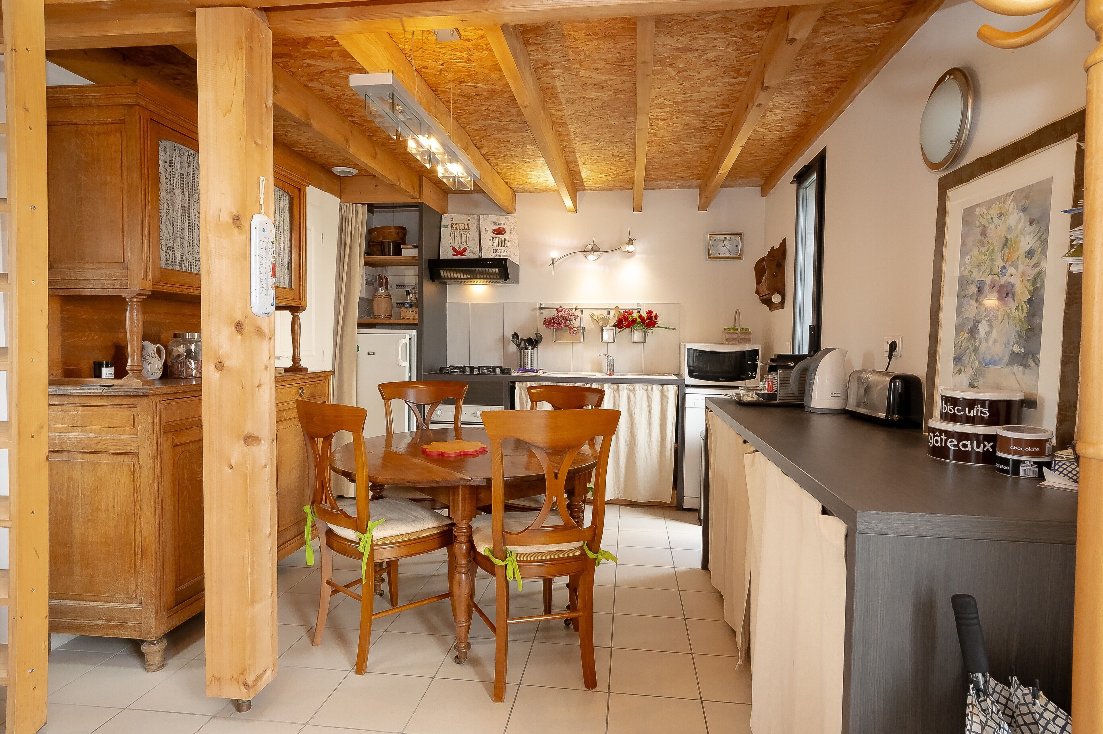 Interior em madeira com mesa e cadeiras de jantar, área de cozinha com eletrodomésticos e balcão com alimentos.