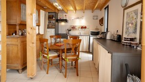 A wooden interior with a dining table and chairs, a kitchen area with appliances, and a counter with food items. - Holiday Home 'Le Balcon Des Bauges' with Mountain View, Shared Pool and Wi-Fi (LA MOTTE-SERVOLEX)