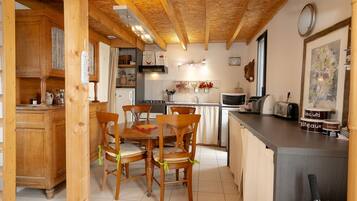 Interior em madeira com mesa e cadeiras de jantar, área de cozinha com eletrodomésticos e balcão com alimentos.