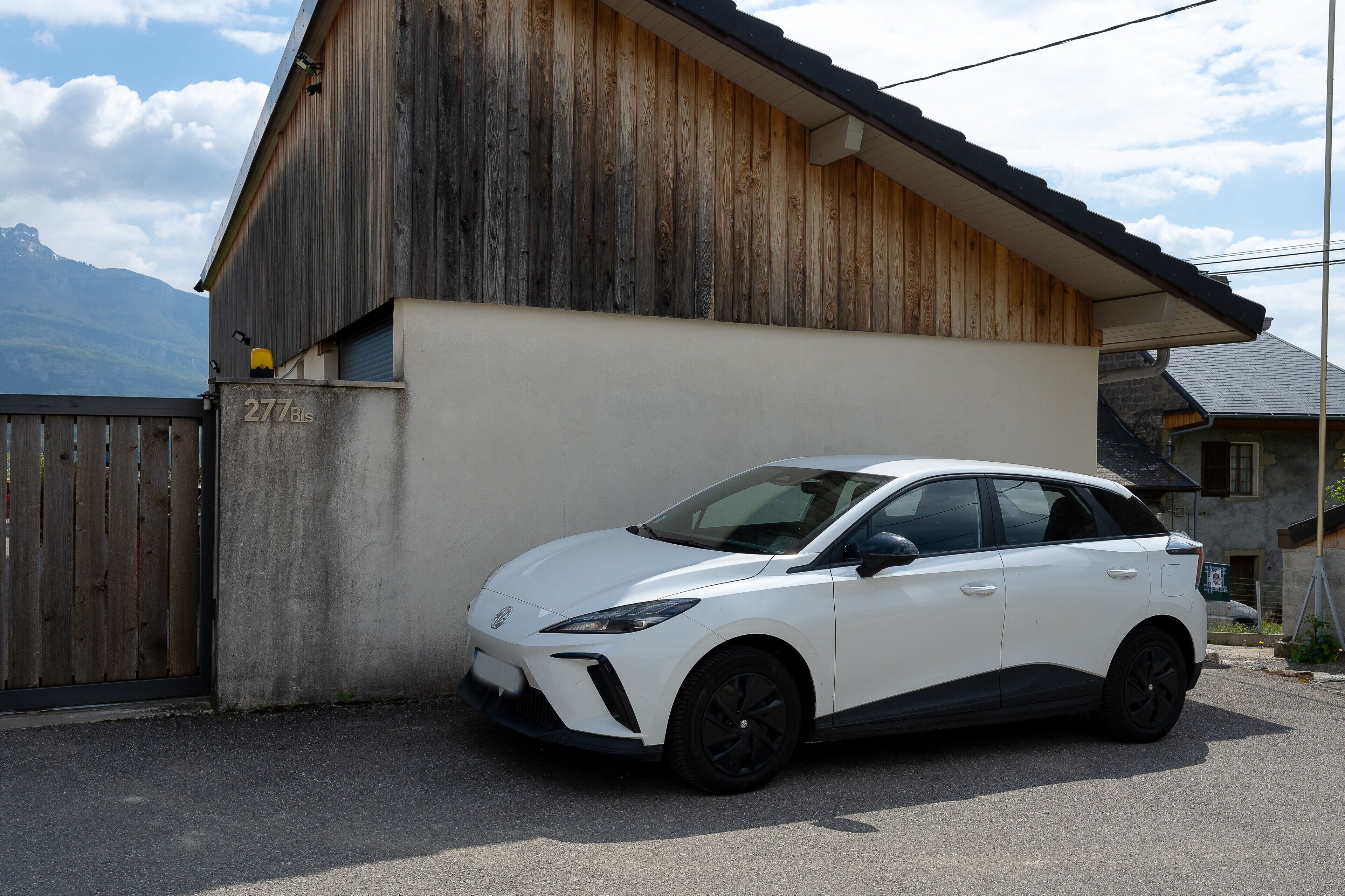 Un VUS blanc est garé devant un bâtiment en bois, doté d’un mur en béton et d’un portail en métal.