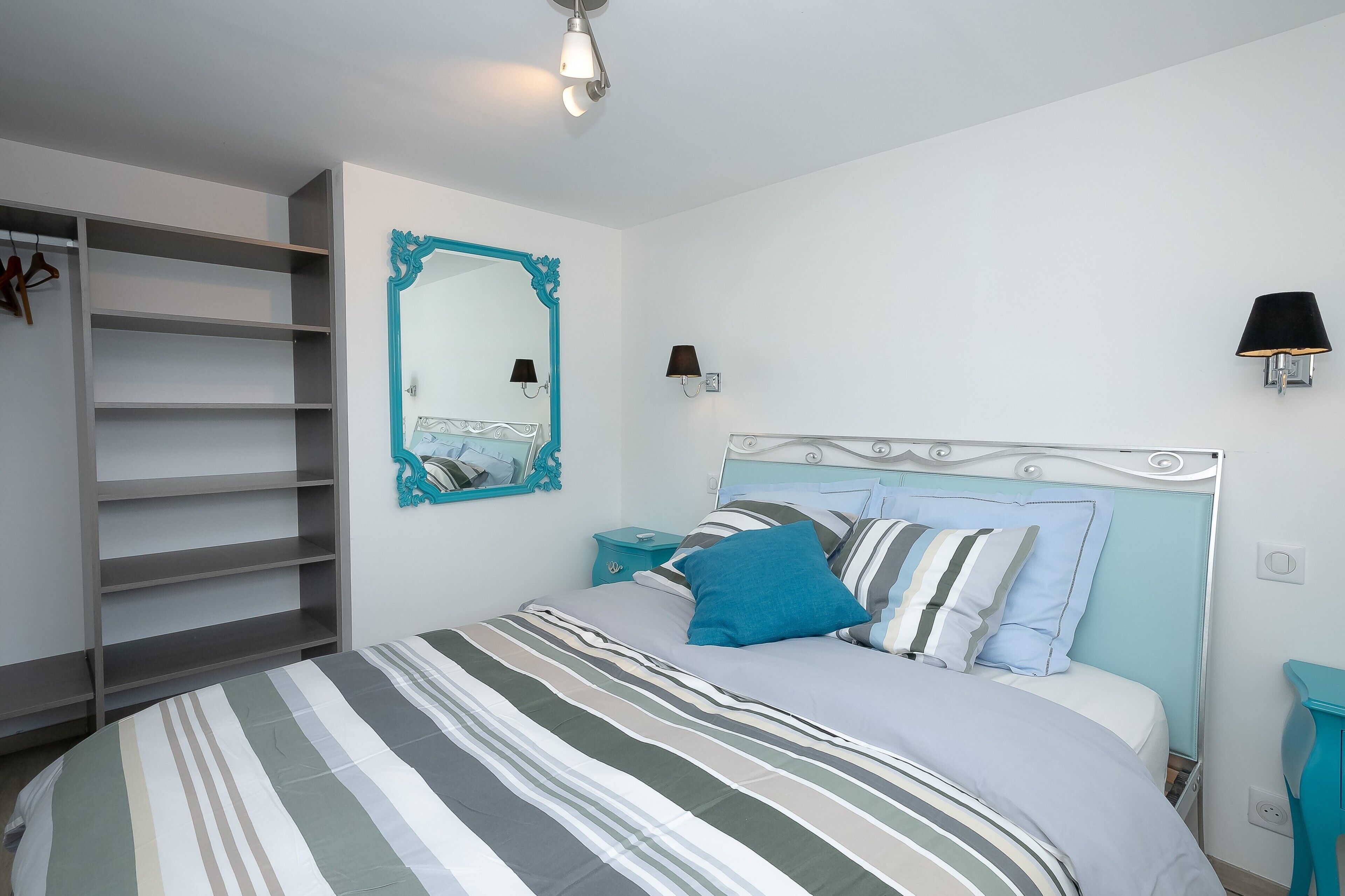 A bedroom with a bed, a wardrobe, a mirror, and wall-mounted lights.