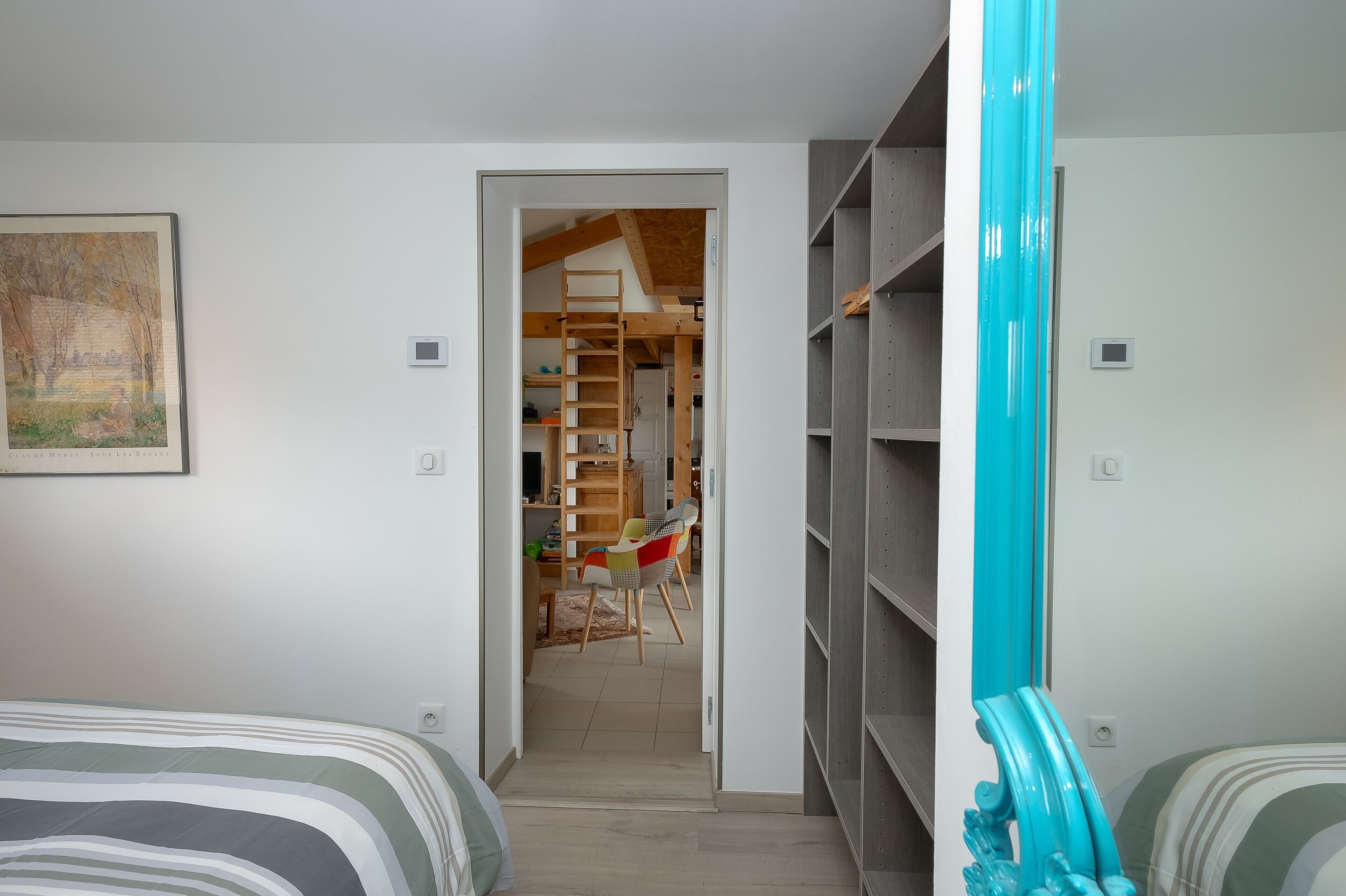 A bedroom with a bed, a chair, a wardrobe, and a door leading to a hallway.