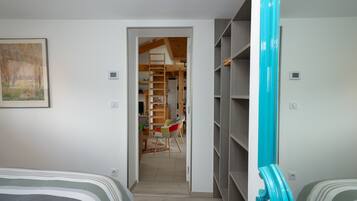 Um quarto com cama, cadeira, guarda-roupa e porta que dá para um corredor.