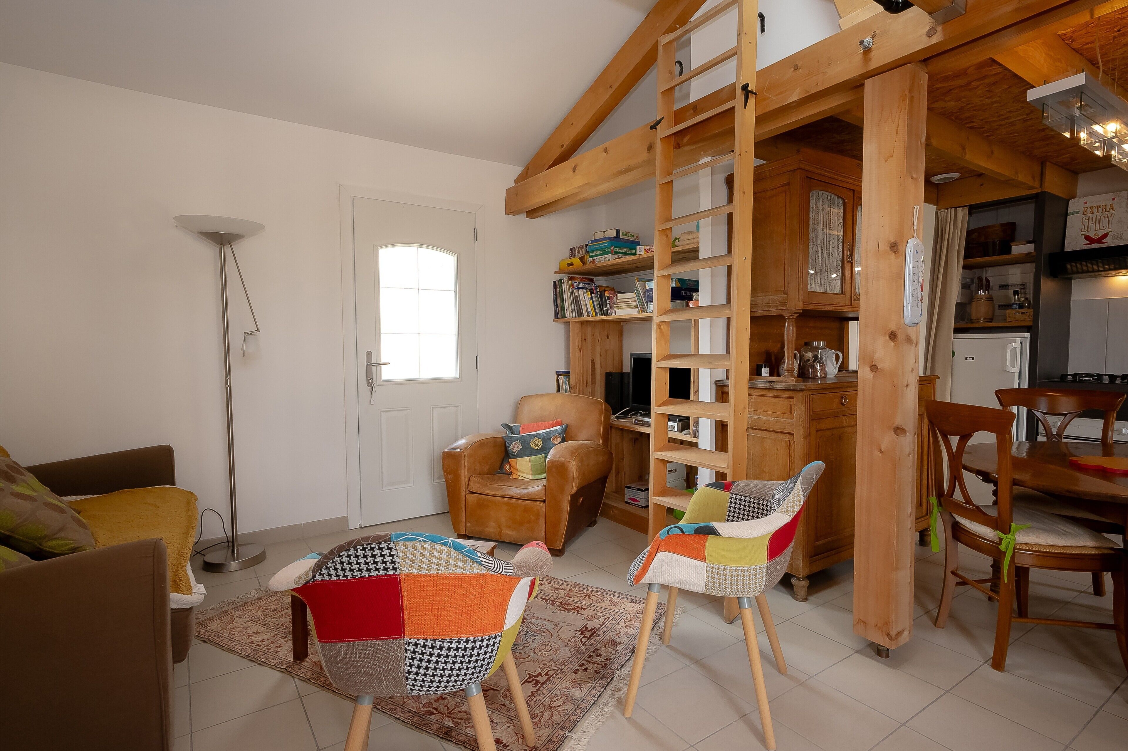 Een woonkamer met een houten ladder, een boekenkast, een eethoek met stoelen en een vloerlamp.