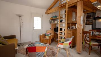 Een woonkamer met een houten ladder, een boekenkast, een eethoek met stoelen en een vloerlamp.