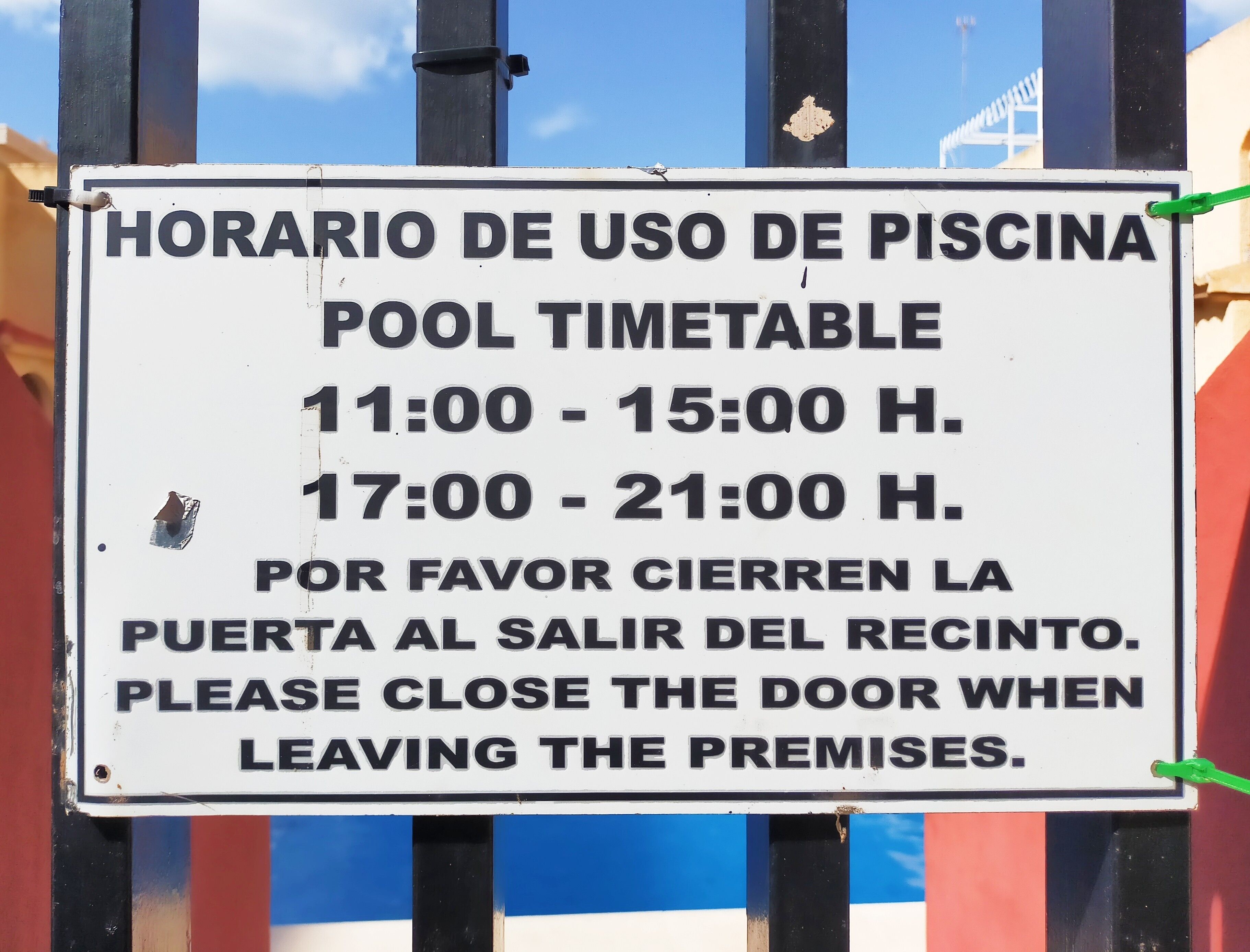 Cartel con el horario de la piscina, indicando los horarios de funcionamiento y un aviso para cerrar la puerta al salir.