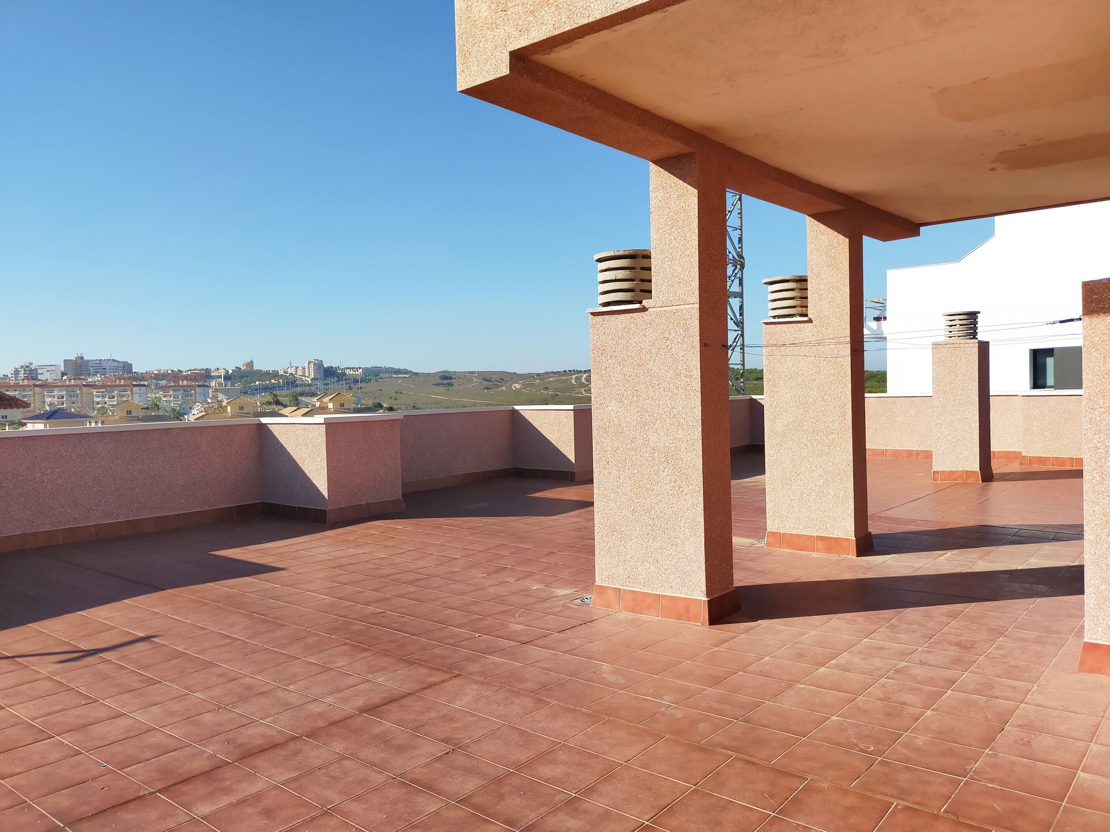 Une terrasse sur le toit offrant une vue dégagée sur le paysage urbain, avec un sol carrelé et des colonnes apparentes.