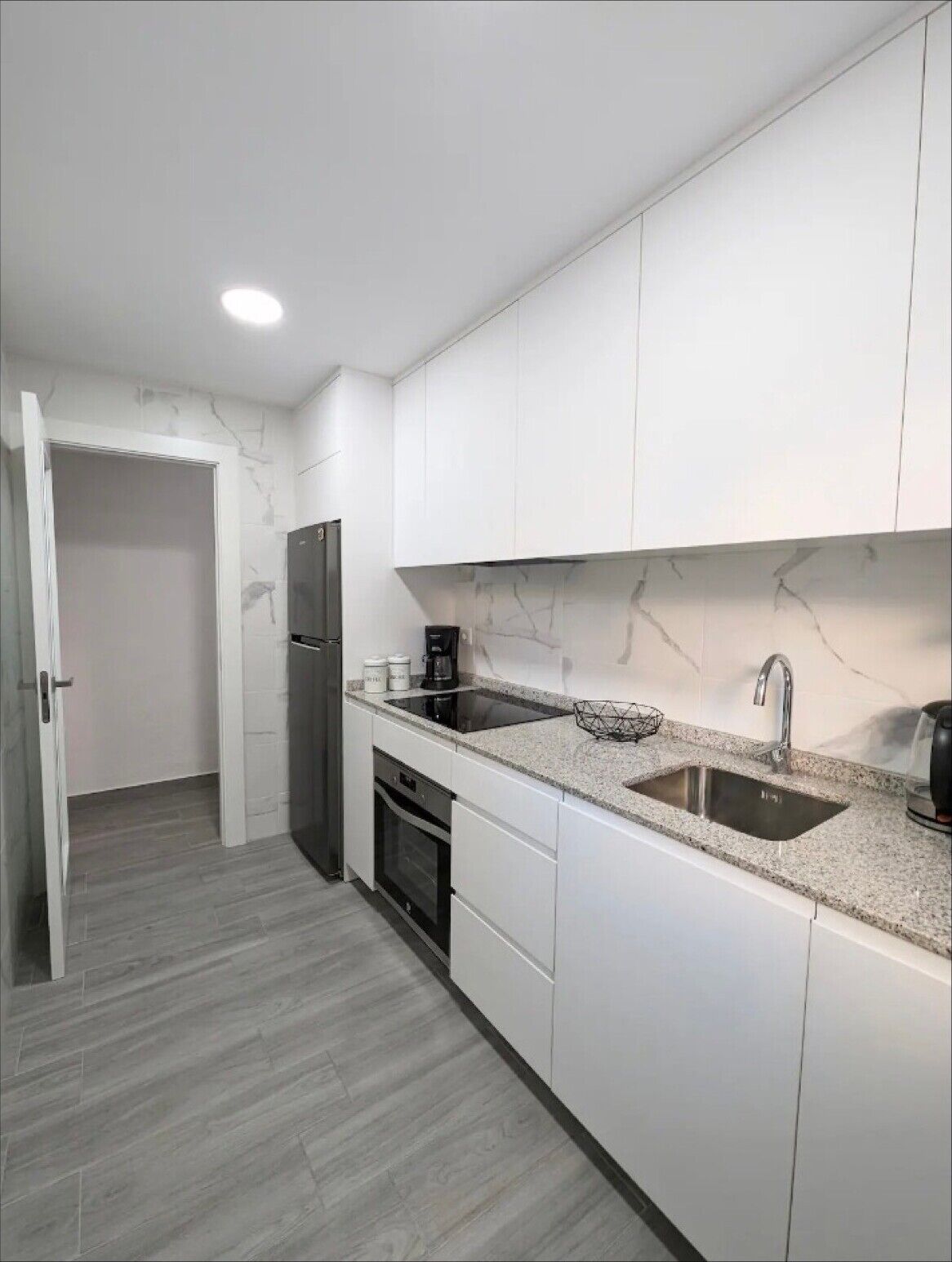 Una cocina moderna con armarios blancos, un lavamanos doble, horno empotrado y refrigerador.