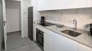 Una cocina moderna con armarios blancos, un lavamanos doble, horno empotrado y refrigerador.