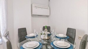 Un comedor con una mesa de vidrio, cuatro sillas grises y un equipo de aire acondicionado blanco en la pared.