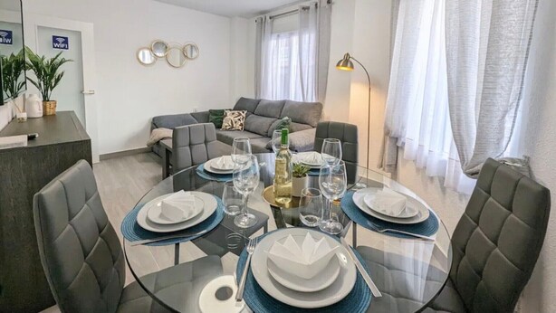Un comedor moderno con una mesa de vidrio dispuesta para cuatro personas, un sofá y una lámpara.