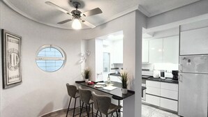 Una cocina moderna con una isla central, taburetes de bar, un ventilador de techo y un refrigerador.