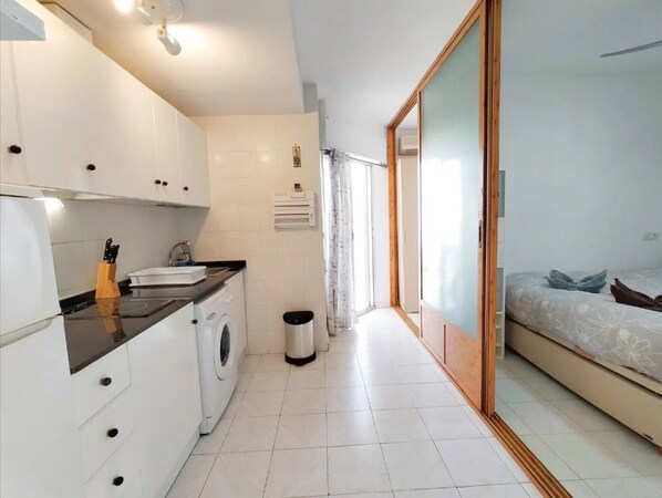 A compact kitchen with a washing machine, a sink, and a small trash bin.