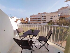 A balcony with a table and chairs, a potted plant, and a view of surrounding buildings.