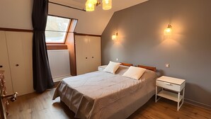 Un dormitorio con cama, mesitas de noche, armario, ventana con cortinas e iluminación en la pared.