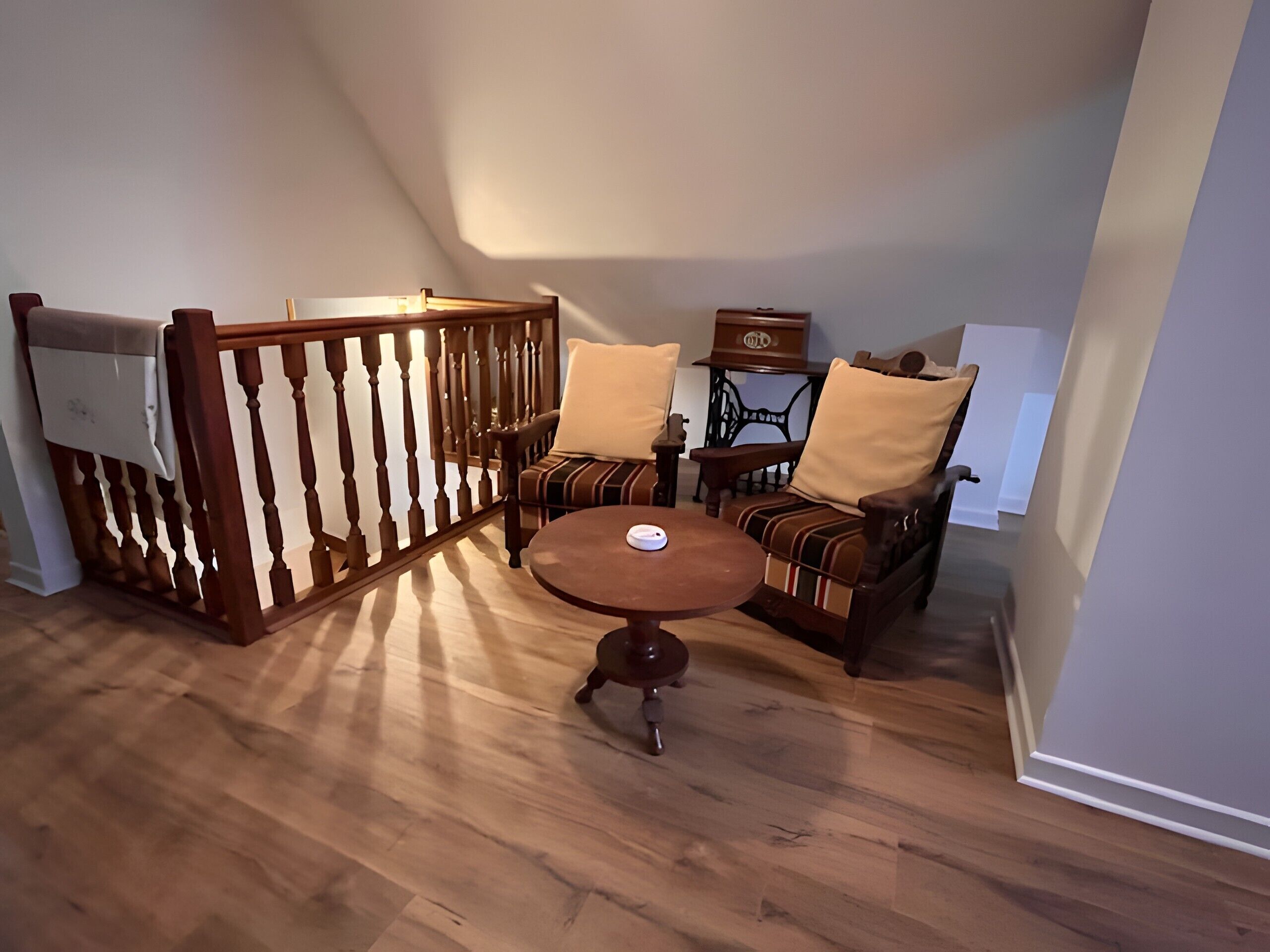 Una habitación con piso de madera, una mesa redonda, dos sillones, una mesita auxiliar y un aparador decorativo.