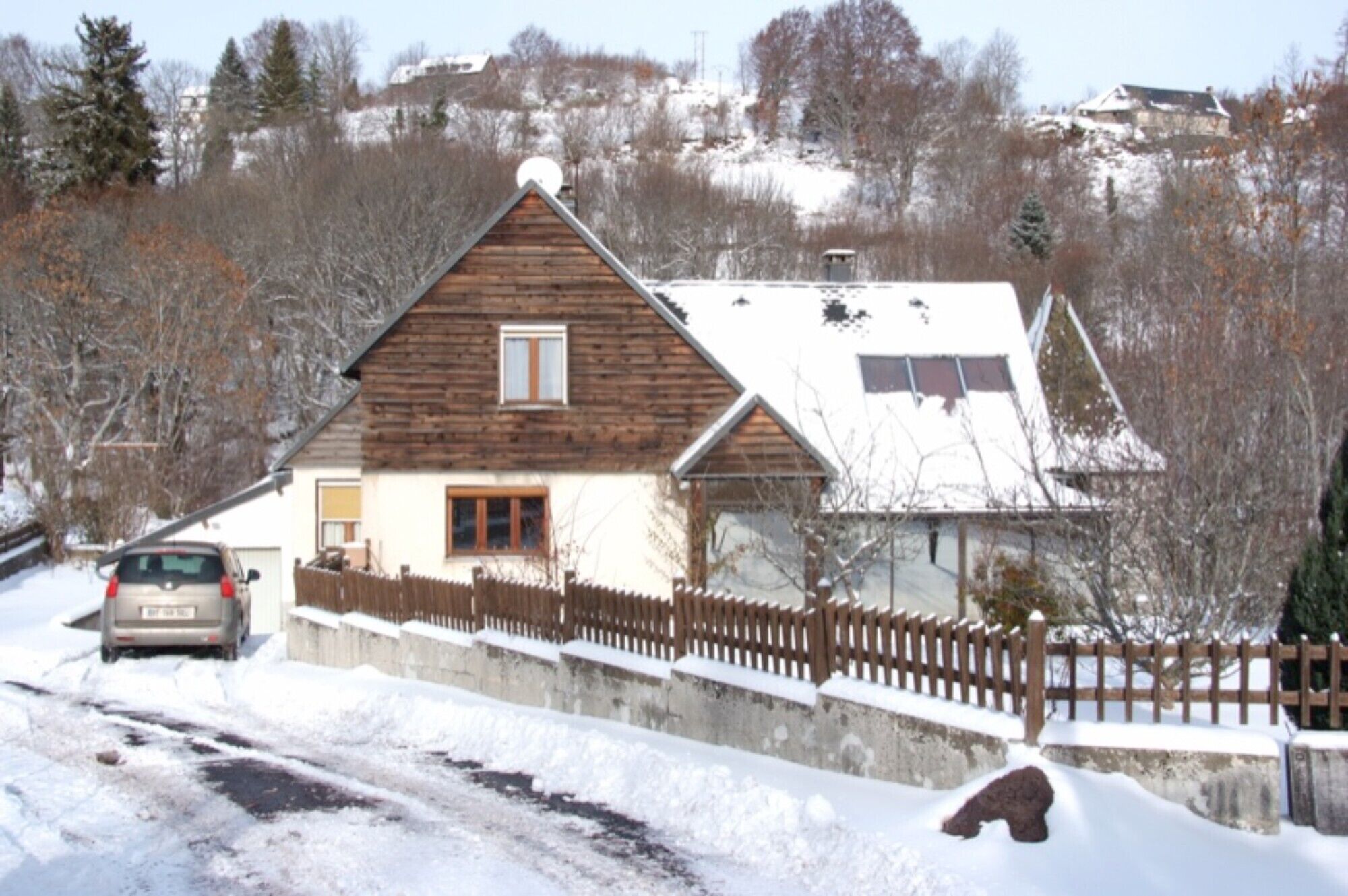 A wooden house with a sloped roof, a visible garage, and a fenced yard.