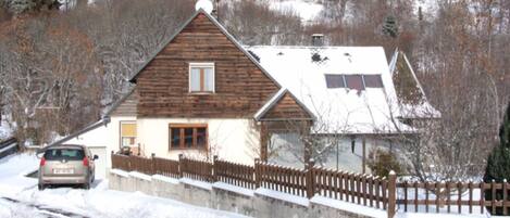 A wooden house with a sloped roof, a visible garage, and a fenced yard.