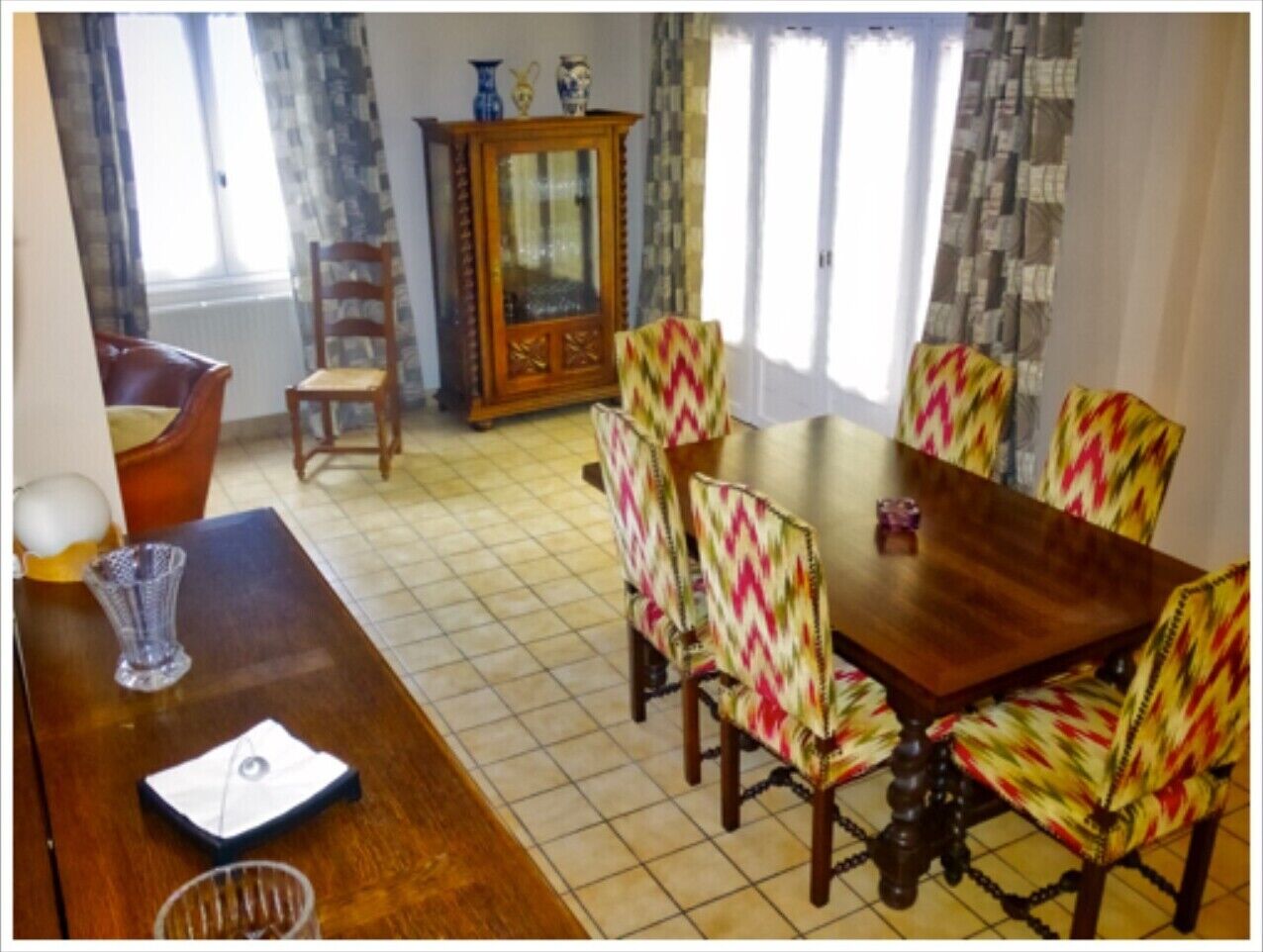 Un coin repas avec une table en bois et des chaises colorées, un buffet et une fenêtre avec des rideaux.