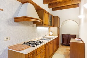 A kitchen with wooden cabinets, a gas stove, and a sink. - Apartment 'Appartamento Trilocale' with Shared Terrace, Shared Garden and Wi-Fi (Bardolino)