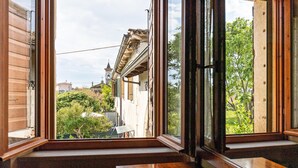 A room with a large window, wooden bench, and a view of buildings and greenery outside. - Apartment 'Appartamento Bilocale' with Shared Terrace, Shared Garden and Wi-Fi (Bardolino)