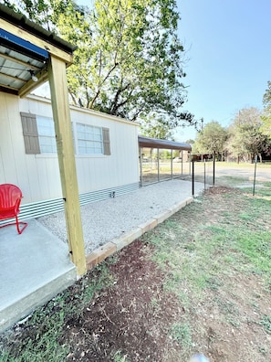 A covered outdoor area with a gravel path leading to a building with windows and a red chair.