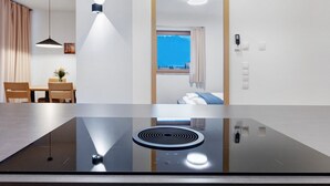 Eine moderne Küche mit einer schwarzen Induktionskochplatte, ein Essbereich mit Holzstühlen und einem Tisch sowie ein Blick auf einen Berg durch ein Fenster.