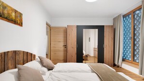 Een slaapkamer met een houten hoofdbord, een bed met witte beddengoed, een houten garderobe en uitzicht door een raam met patroon gordijnen.