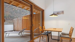 Une pièce avec une table et des chaises en bois, un luminaire suspendu et une porte-fenêtre coulissante donnant sur un espace extérieur.