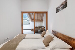 Un dormitorio con cama, almohadas, cabecera de madera y vistas a un balcón y zona exterior.