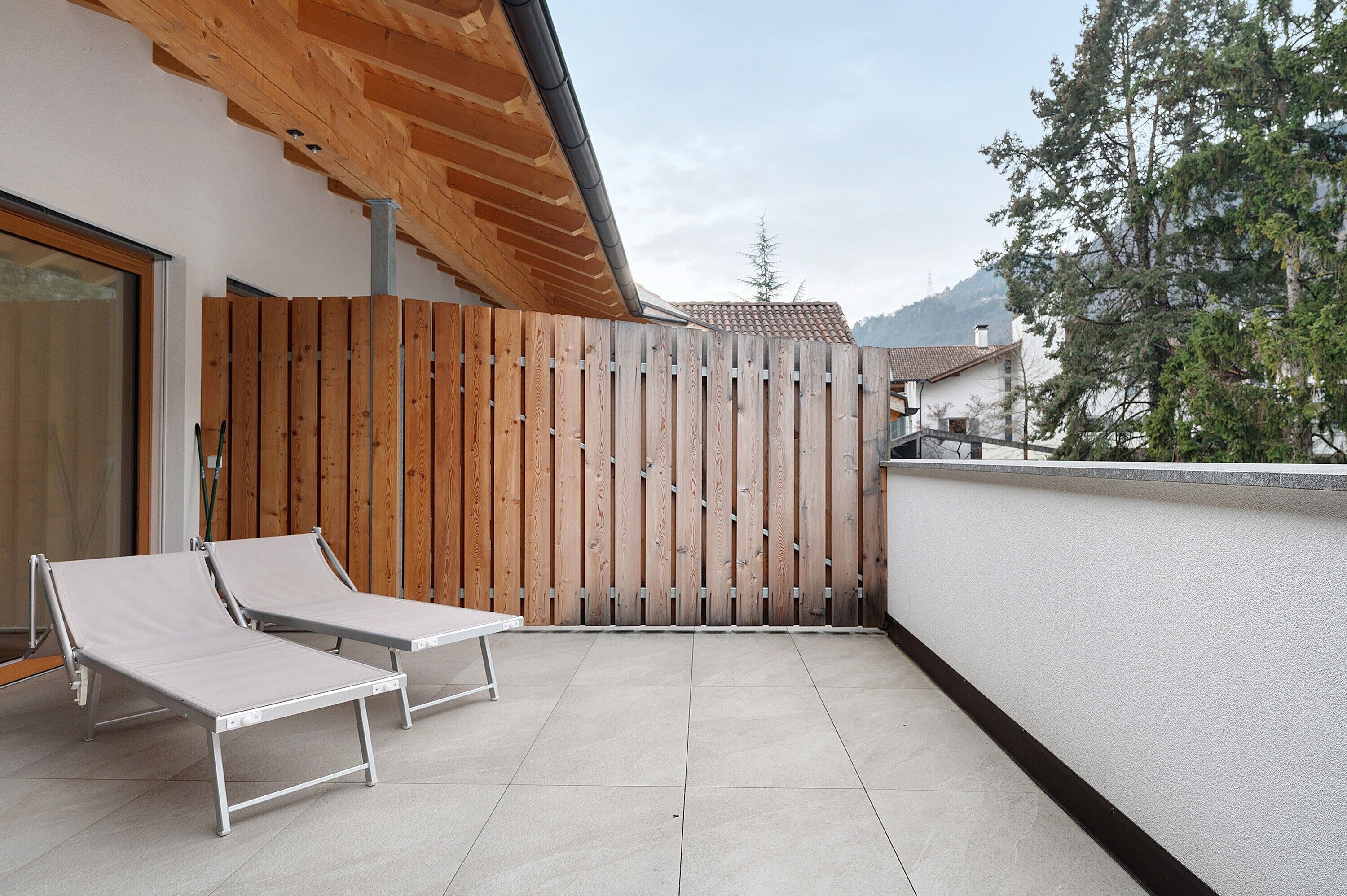 Een balkon met twee witte loungestoelen, een houten hek en uitzicht op een berg.