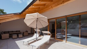 Un espace de détente extérieur moderne, doté de chaises longues, d’une table et d’un parasol.