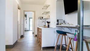 A modern kitchen with a central island, bar stools, a TV mounted on the wall, and a visible door leading to another room. - Casale Lorenzo - Apartment 1 with Private Terrace, Shared Garden and Air Conditioning (Orbetello)