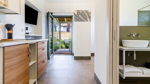 A modern kitchen with wooden cabinets, a flat-screen TV, and a dining area visible through an open door. - Casale Lorenzo - Apartment 1 with Private Terrace, Shared Garden and Air Conditioning (Orbetello)