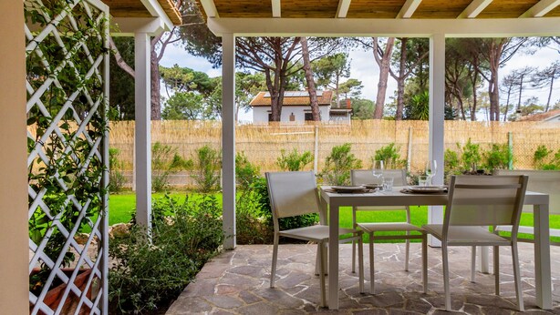 An outdoor patio with stone flooring, a table with chairs, and a view of a house in the background. - Casale Lorenzo - Apartment 1 with Private Terrace, Shared Garden and Air Conditioning (Orbetello)