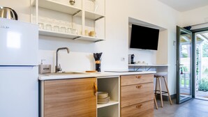 A modern kitchen with white cabinetry, a built-in stove, and a flat-screen TV mounted above the counter. - Casale Lorenzo - Apartment 1 with Private Terrace, Shared Garden and Air Conditioning (Orbetello)