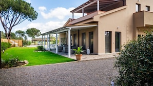 A modern house with a covered patio, a well-maintained lawn, and a gravel driveway. - Casale Lorenzo - Apartment 2 with Private Terrace, Shared Garden and Air Conditioning (Orbetello)
