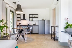 A modern kitchen with a dining area, clear chairs, a hanging light fixture, and a potted plant.