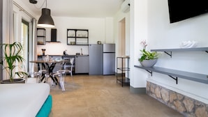 A modern kitchen with a dining area, a TV mounted on the wall, and a stone accent wall. - Casale Lorenzo - Apartment 2 with Private Terrace, Shared Garden and Air Conditioning (Orbetello)