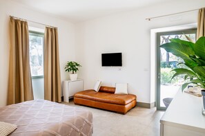 A modern hotel room with a bed, a sofa, a TV, a plant, and a sliding glass door. - 'Casale Lorenzo - Room 3' with private veranda, shared garden and air conditioning (Orbetello)