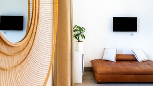 Una sala de estar moderna con un sofá, dos televisores fijos en la pared, una planta en maceta y un sillón de mimbre.
