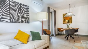 A modern living room with a sofa, a dining table with chairs, a lamp, and a painting on the wall. - Casale Lorenzo - Apartment 4 with private terrace, shared garden and air conditioning (Orbetello)