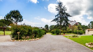 A gravel driveway leading to a building with a covered area on the left and a grassy area with trees and shrubs on the right. - Casale Lorenzo - Apartment 4 with private terrace, shared garden and air conditioning (Orbetello)